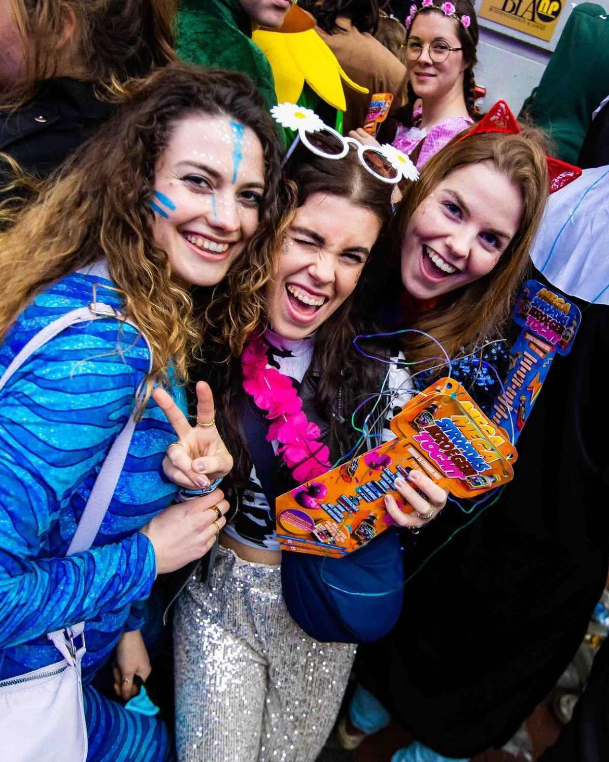 Drie vriendinnen met glitter en schmink, een van hen houdt een mega das vast