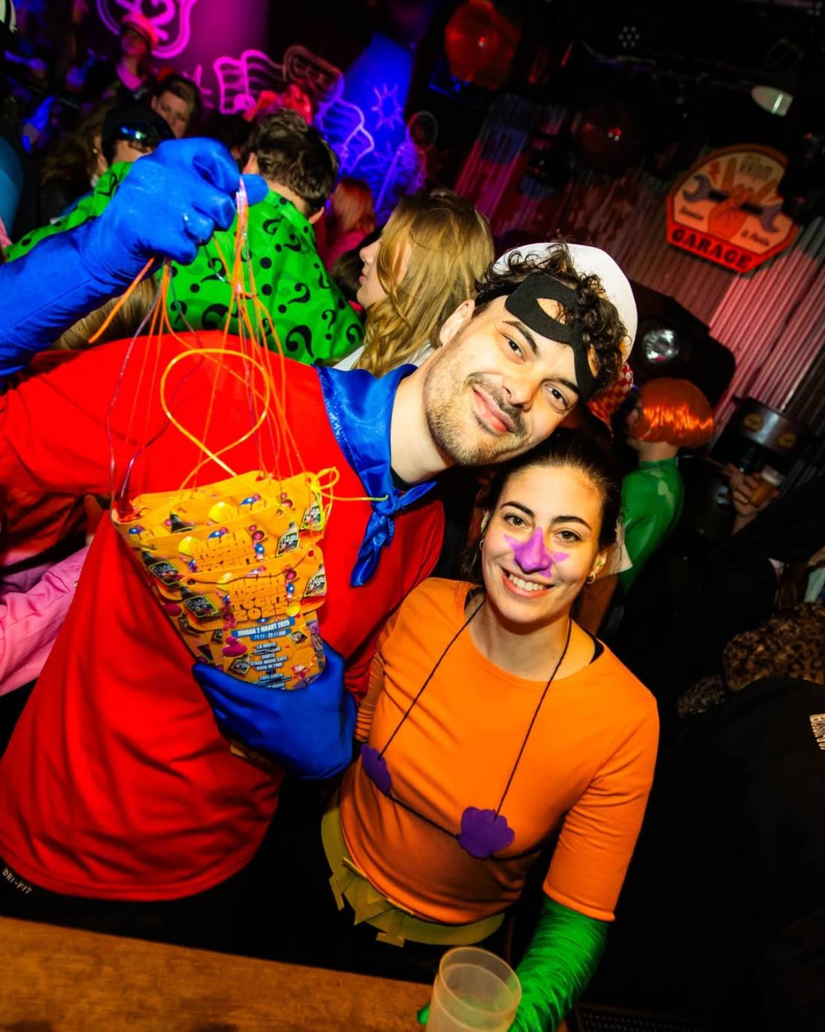 Stel in superheldenkostuum aan de bar, hij houdt een stapel stropdassen omhoog